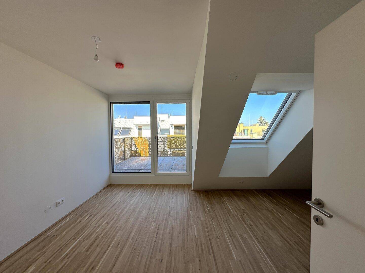 Schlafzimmer mit Parkettboden, großen Fenstern und direktem Zugang zur sonnigen Terrasse.