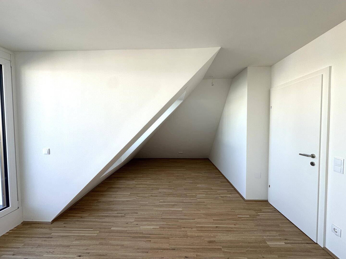 Geräumiges Schlafzimmer mit Parkettboden und schräger Wand, bietet vielseitige Einrichtungsmöglichkeiten.
