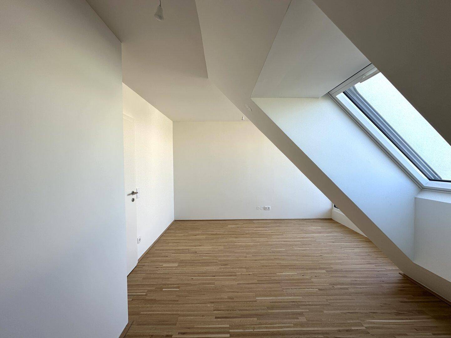 Schlafzimmer mit Parkettboden und schrägen Dachfenstern, die viel natürliches Licht hereinlassen.