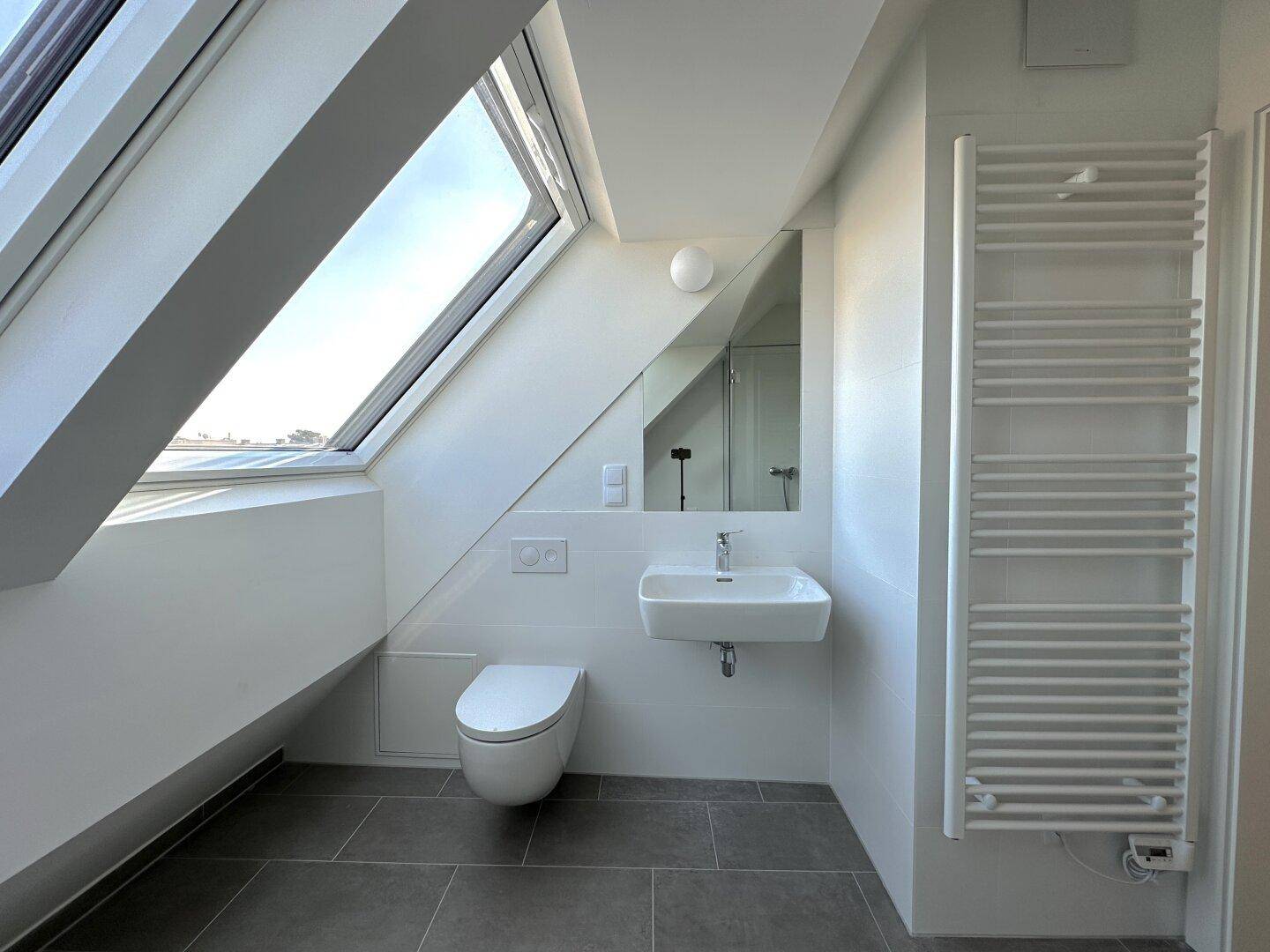 Helles Badezimmer mit Waschbecken, WC, Dachschräge und praktischem Handtuchheizkörper.