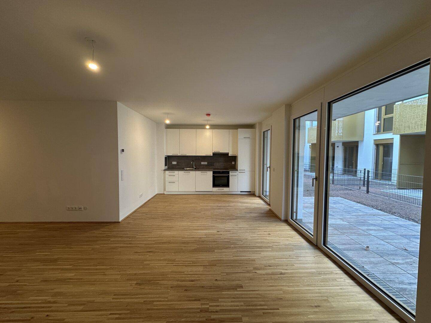 Heller offener Wohnbereich mit integrierter Küche, Parkettboden und großen Fenstern zur Terrasse.
