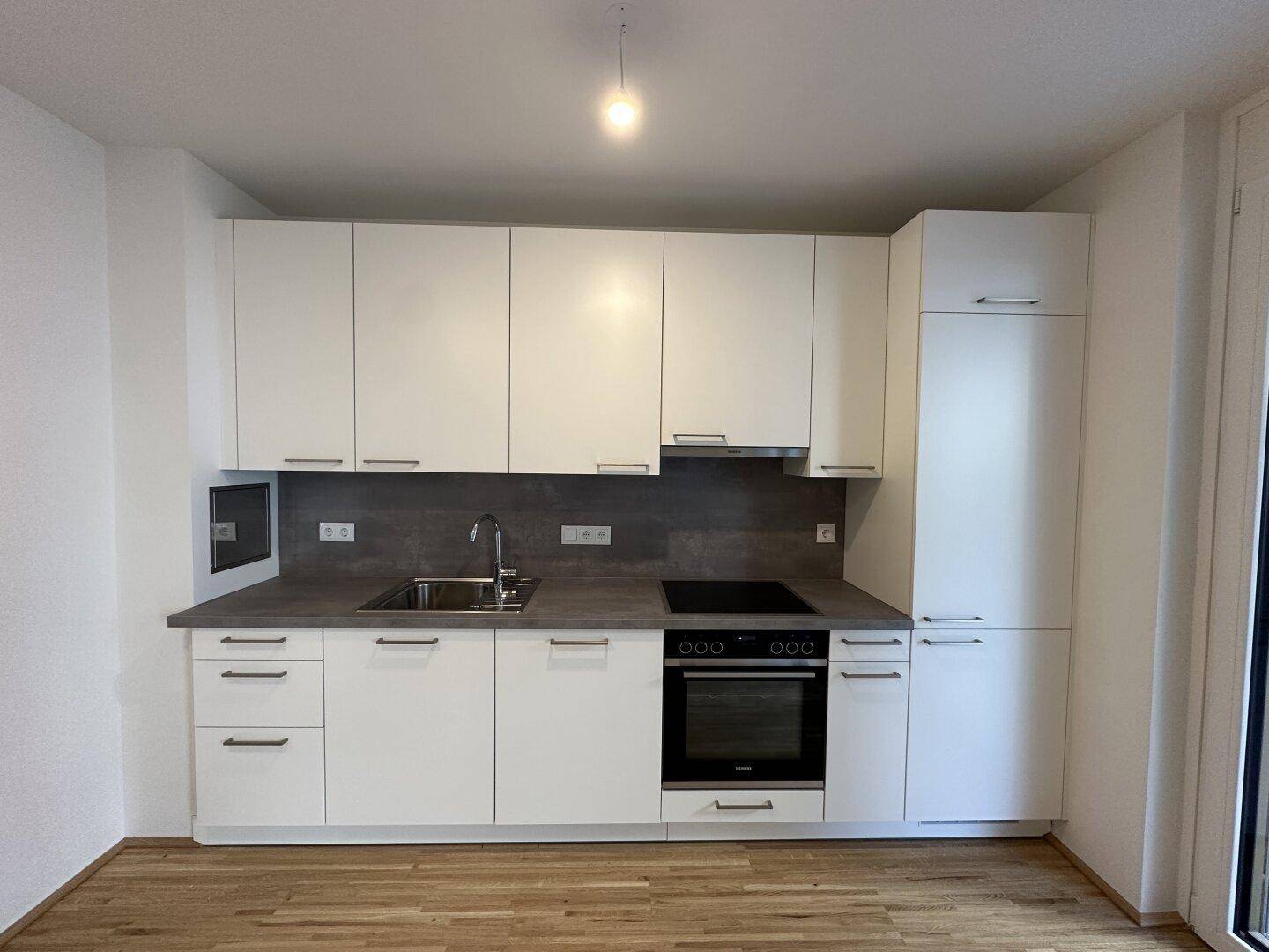 Moderne weiße Einbauküche mit dunkler Arbeitsplatte, integriertem Backofen und Induktionskochfeld.