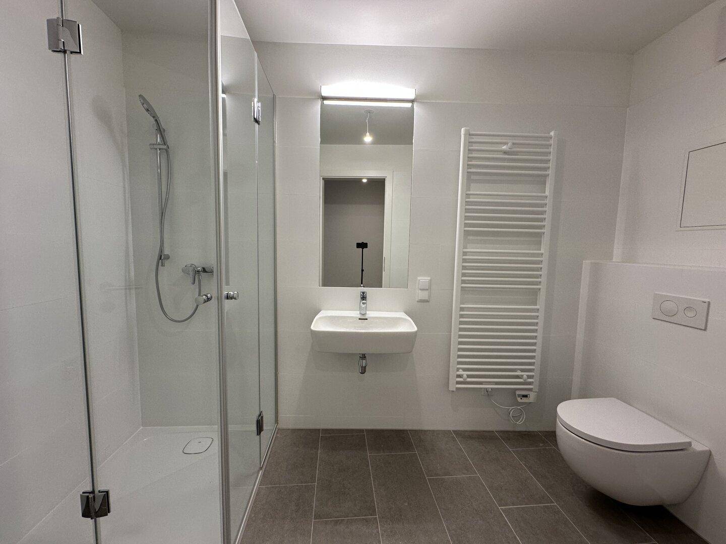 Modernes Badezimmer mit ebenerdiger Glasdusche, Wand-WC und beheiztem Handtuchhalter.
