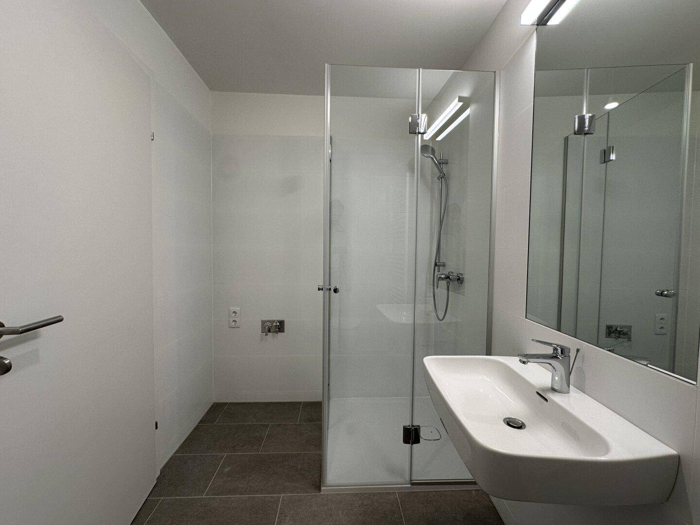 Zeitgemäßes Badezimmer mit Glasdusche, Waschbecken, großem Spiegel und Fliesenboden.