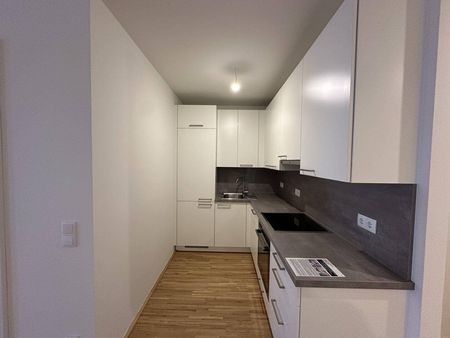 Schmale, moderne Küche mit weißen Schränken, dunkler Arbeitsplatte und Parkettboden.