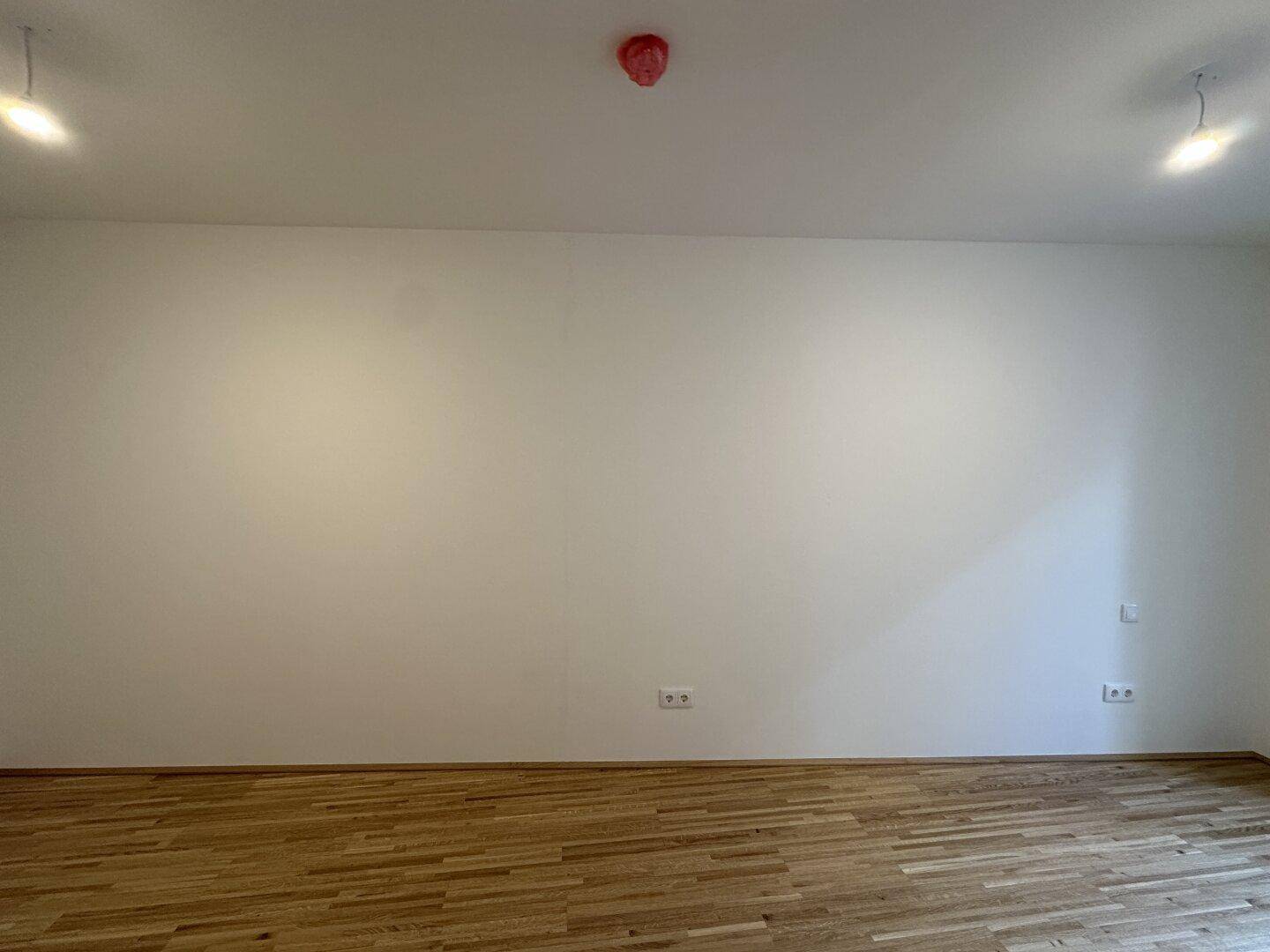 Leere Wand in einem Zimmer mit Parkettboden und Steckdosen.