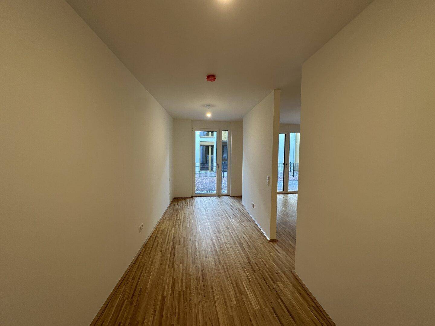 Langer Flur mit Parkettboden und Zugang zu einem Außenbereich durch eine Glastür.