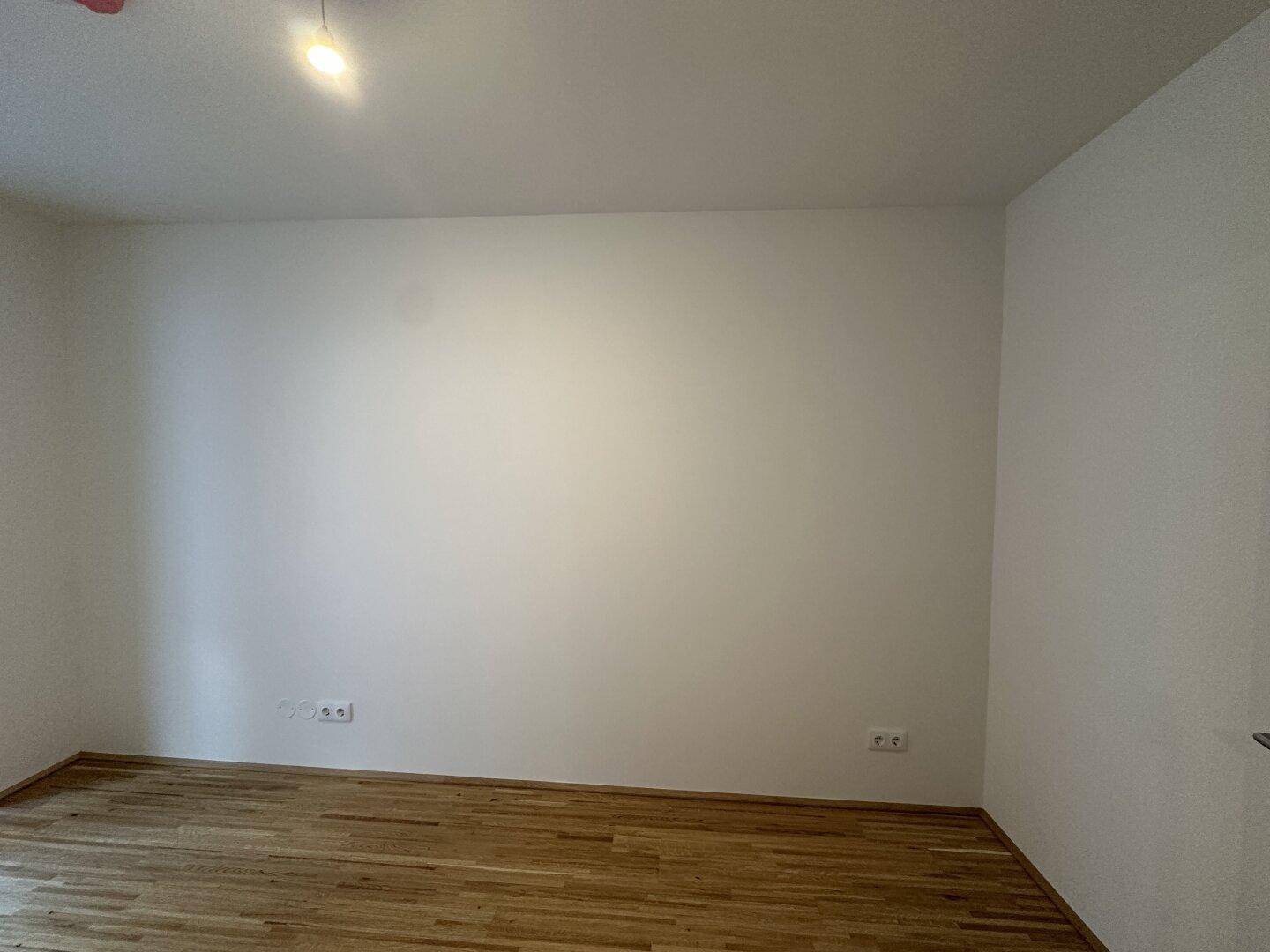 Leere Wand in einem Zimmer mit Parkettboden und Steckdosen.