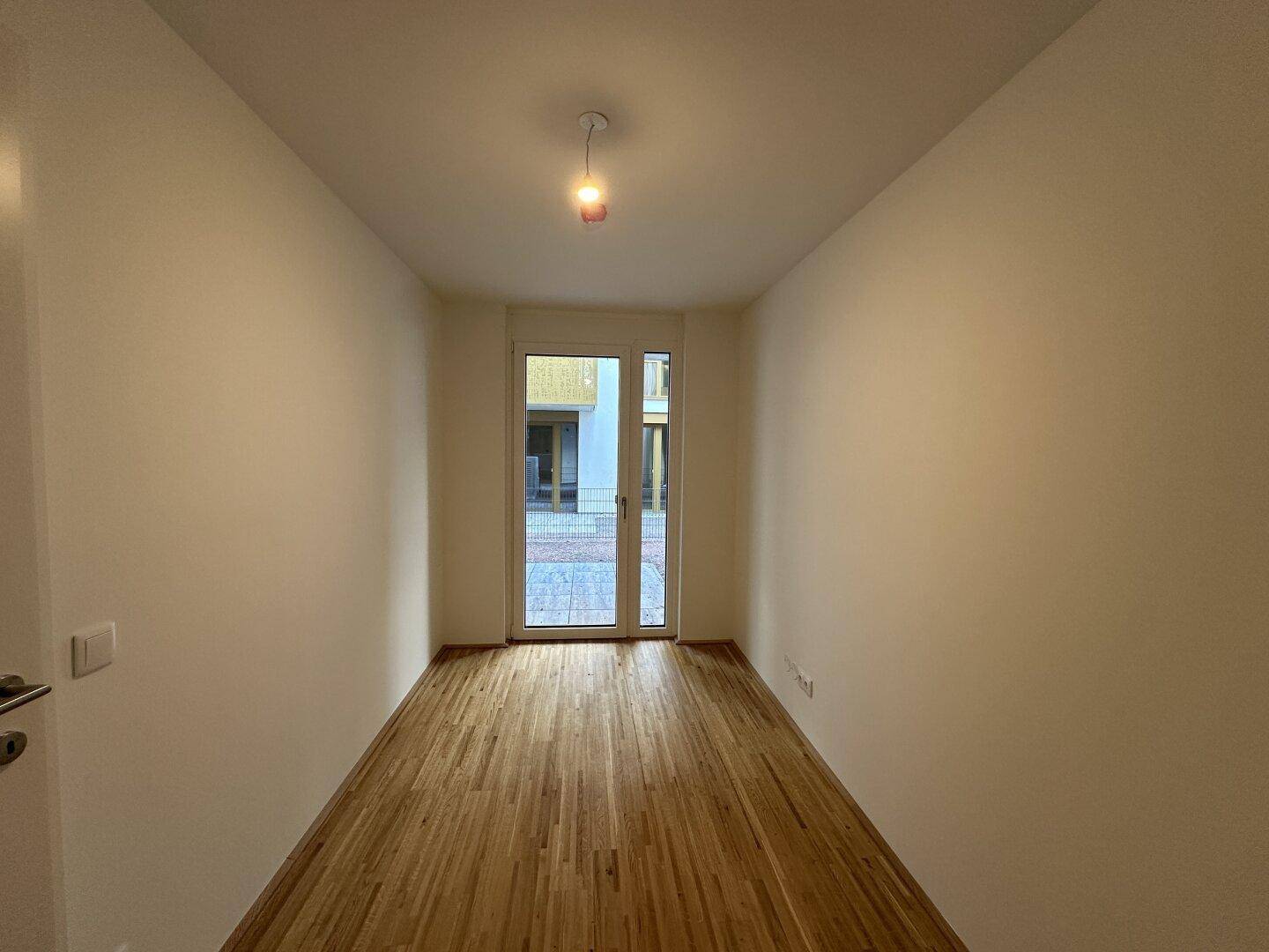 Kleines Zimmer mit Parkettboden und Glastür, die nach draußen führt.