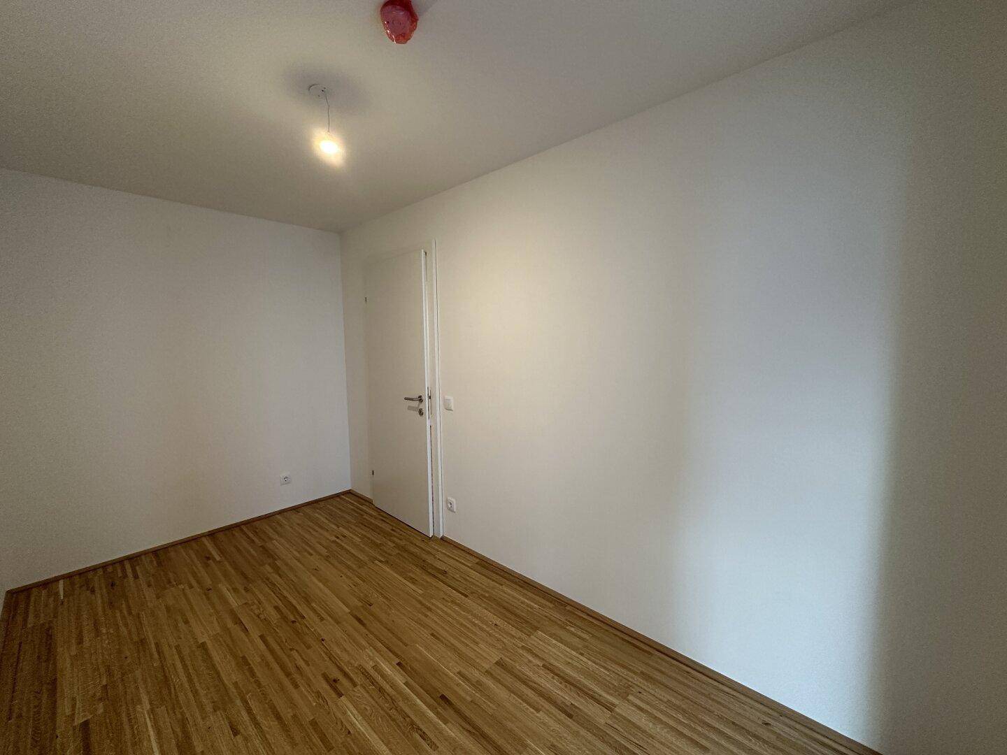 Leeres Zimmer mit Parkettboden und weißer Tür, bereit zur individuellen Gestaltung.