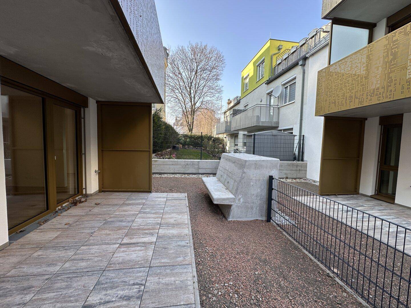 Private Terrasse mit Steinplatten, Betonbank und kleinem Gartenbereich.