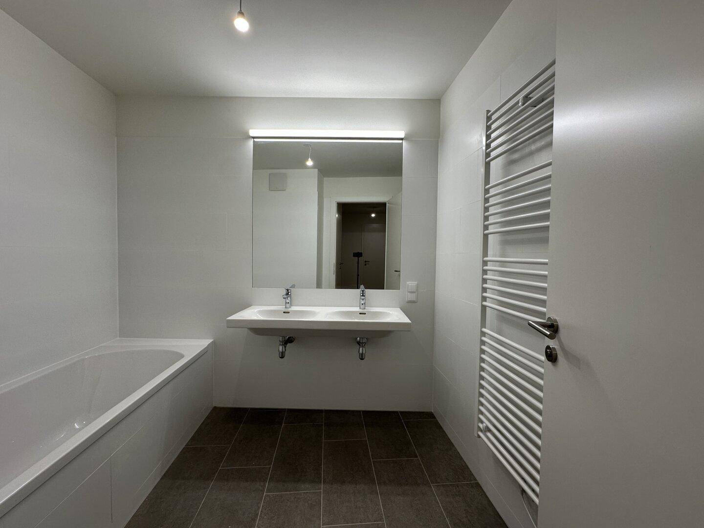 Modernes Badezimmer mit Doppelwaschbecken, Badewanne und beheiztem Handtuchhalter.