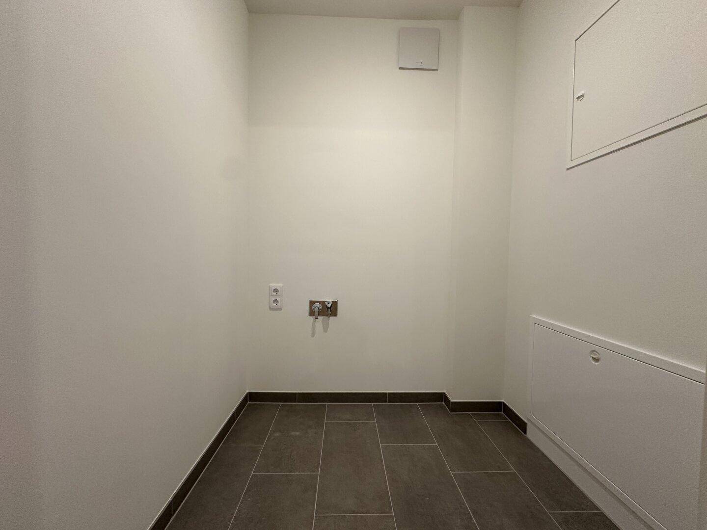 Praktischer Hauswirtschaftsraum mit Fliesenboden und Anschlüssen für Waschmaschine.