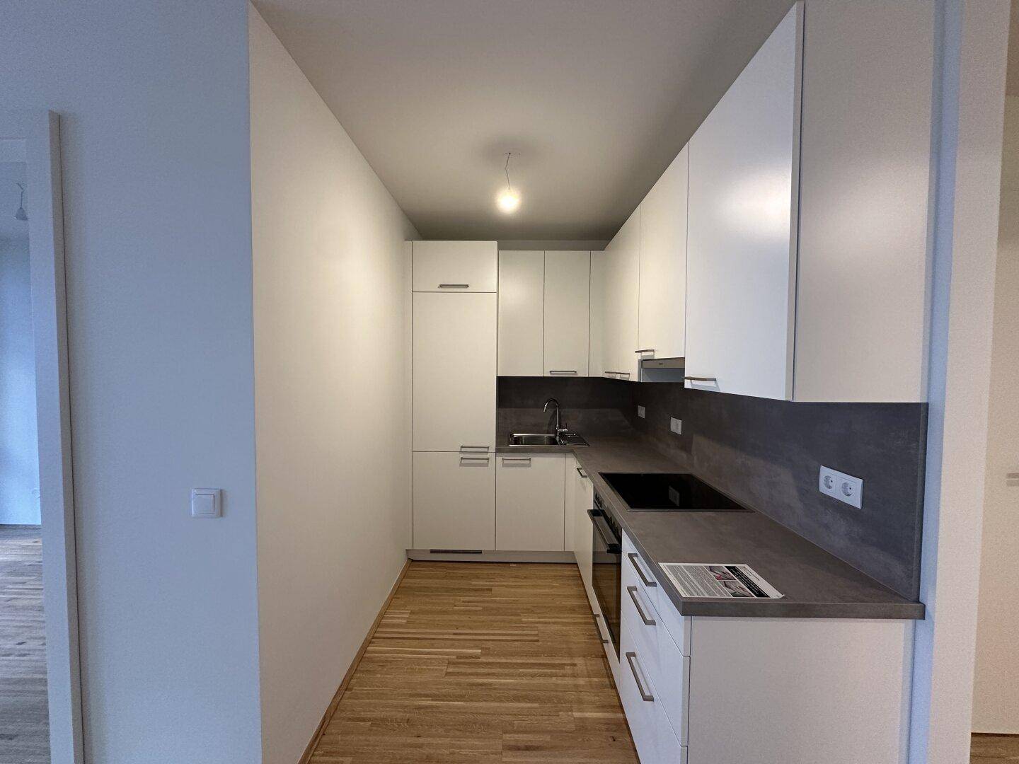Moderne, schmale Küche mit weißen Schränken, dunkler Arbeitsplatte und Holzboden.