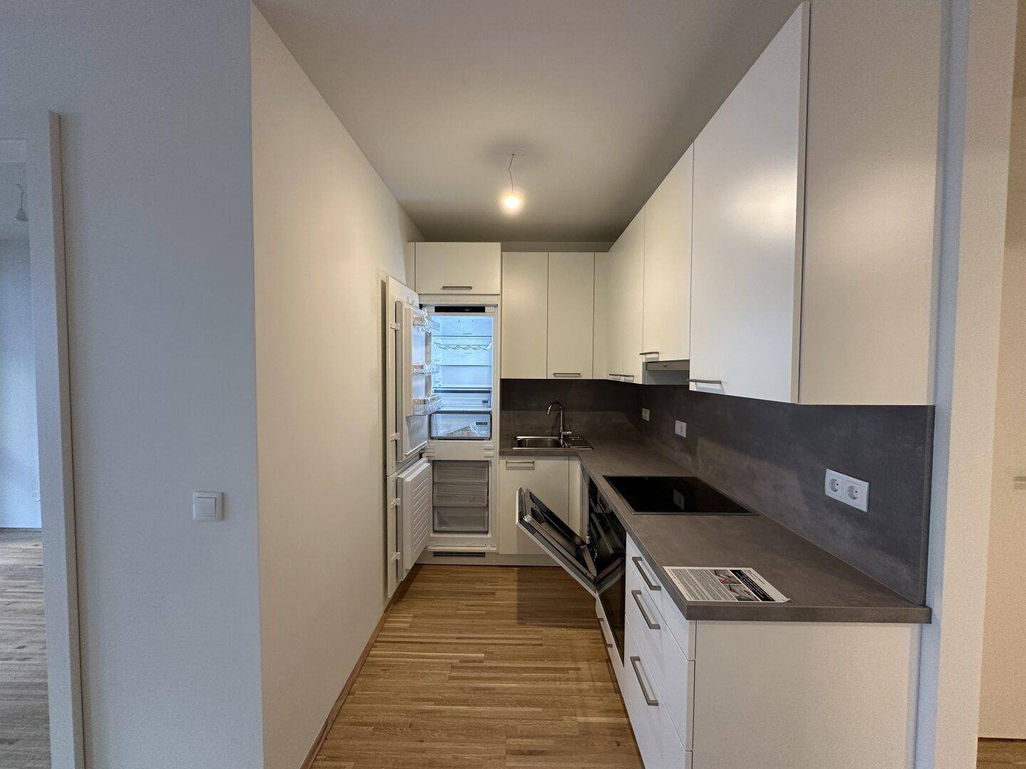 Moderne Einbauküche mit geöffnetem Kühlschrank, weißen Fronten und dunkler Arbeitsplatte.