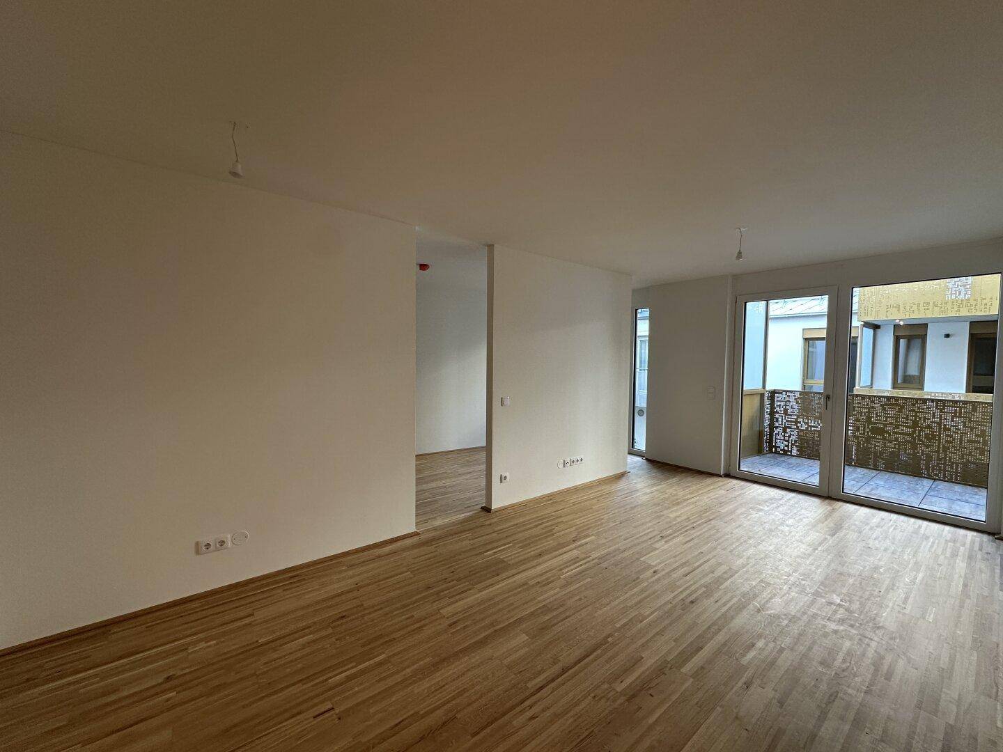 Heller Wohnbereich mit Parkettboden und großen Fenstern, die auf einen Balkon führen.