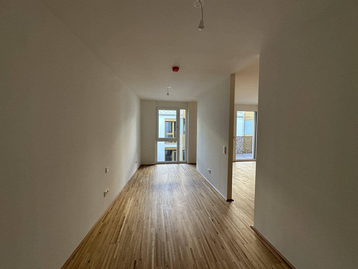 Langer, heller Raum mit Parkettboden und Zugang zu einem Außenbereich, ideal als Wohnzimmer.