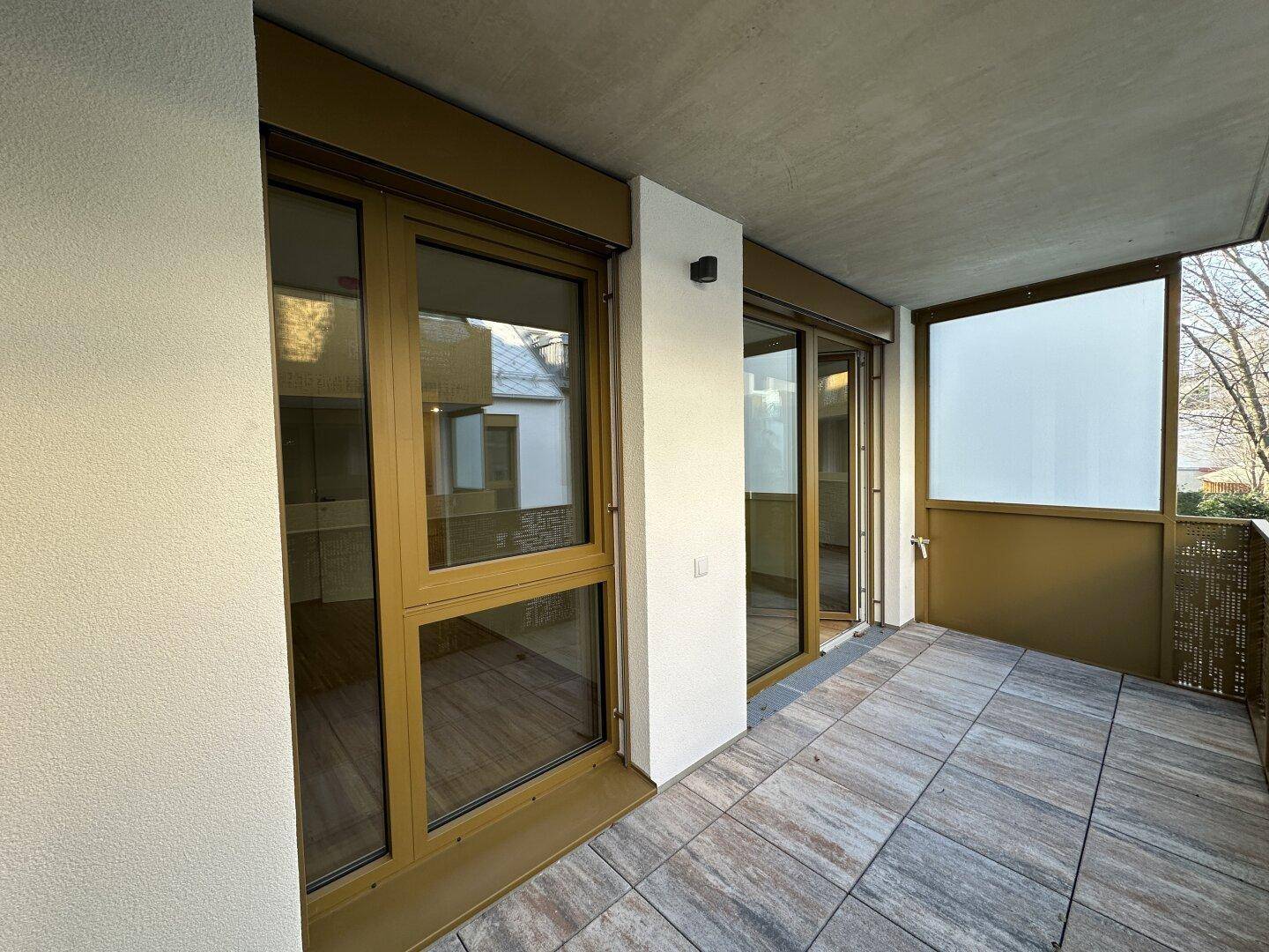 Heller Balkon mit Fliesenboden und großen Fenstern, die viel Tageslicht in die Wohnung lassen.