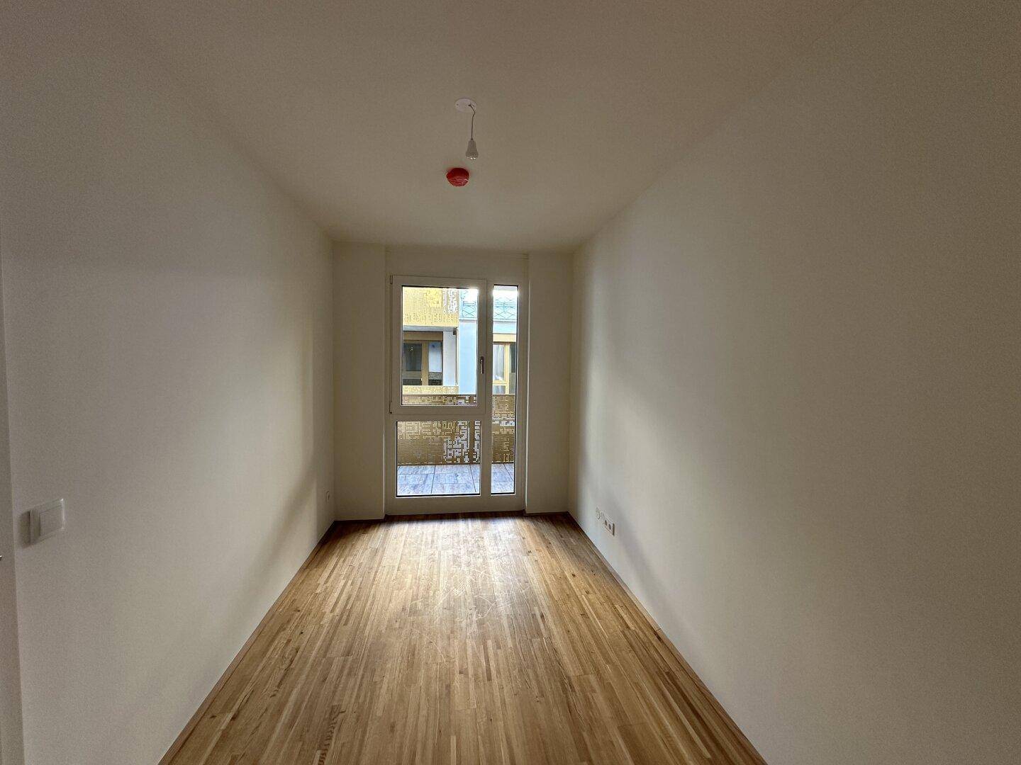 Helles Schlafzimmer mit Parkettboden und Zugang zu einem Balkon, ideal für Ruhe.