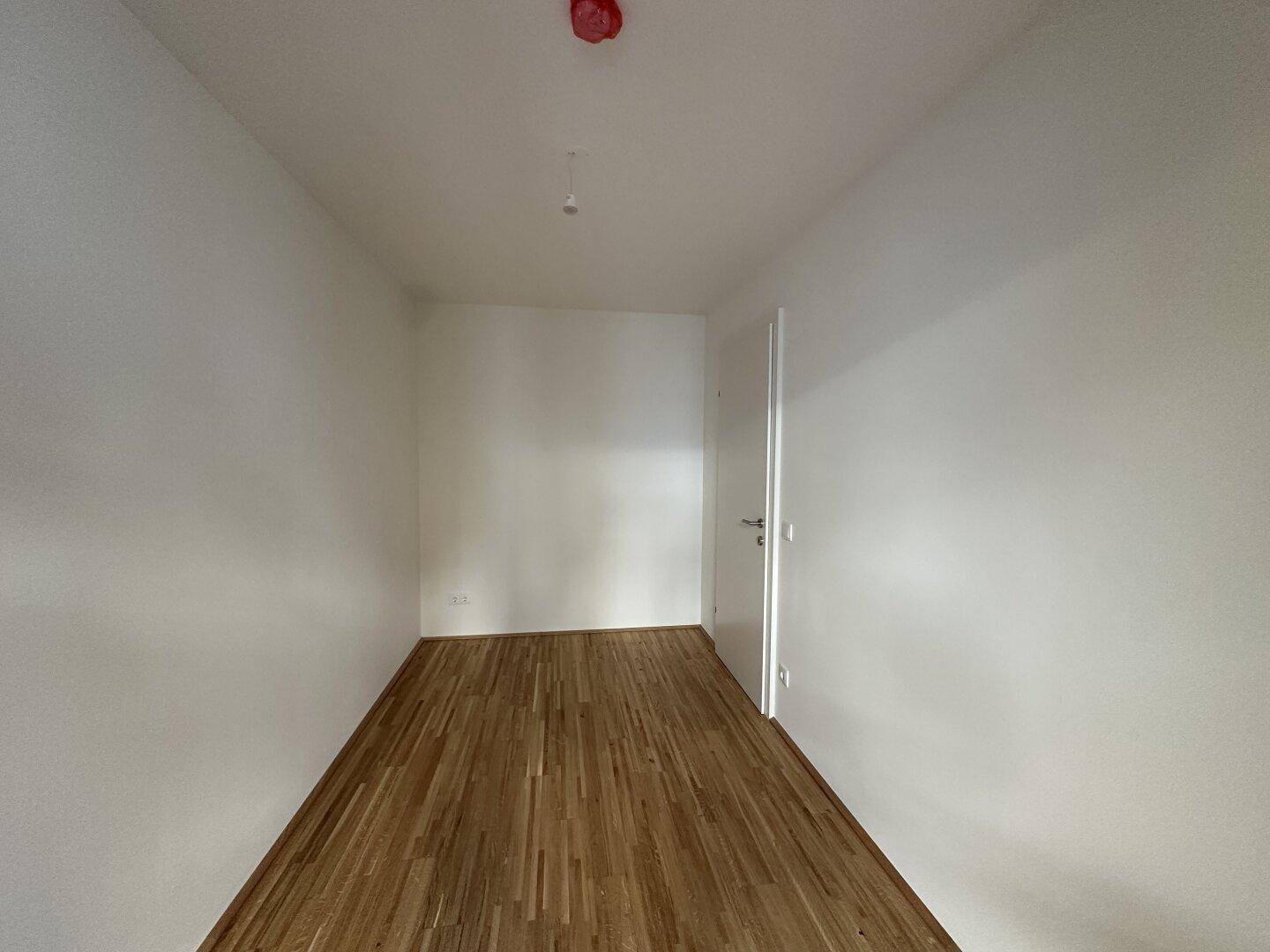 Leerer Raum mit Parkettboden und weißer Tür, bietet Potenzial für Schlaf- oder Arbeitszimmer.