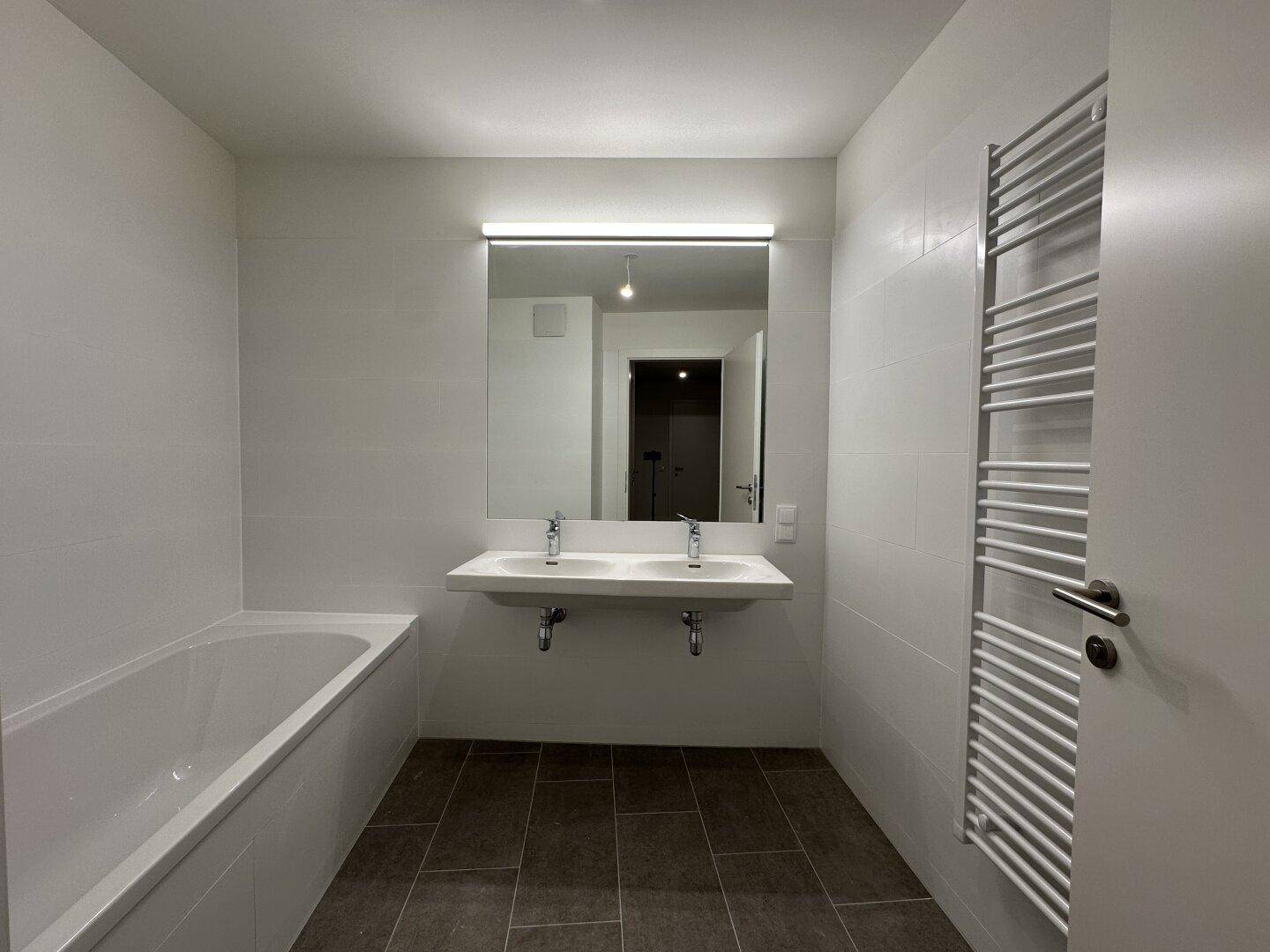 Modernes Badezimmer mit Doppelwaschbecken, Badewanne und beheiztem Handtuchhalter.