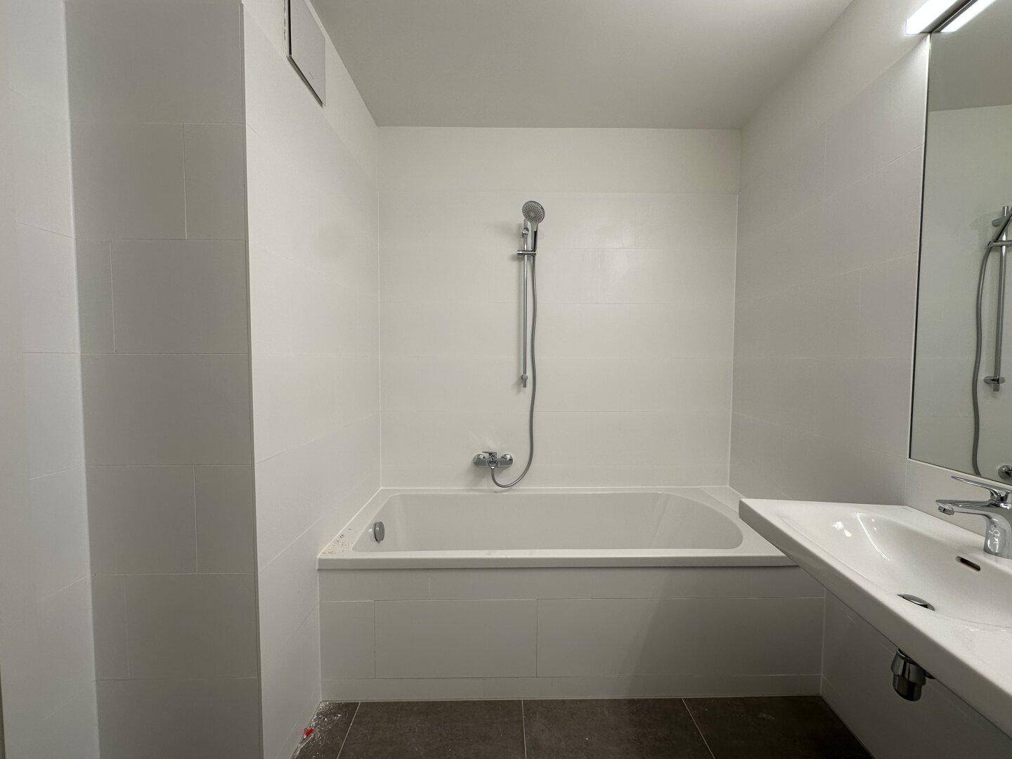 Helles Badezimmer mit Badewanne und Duscharmatur, ausgestattet mit modernen Fliesen.