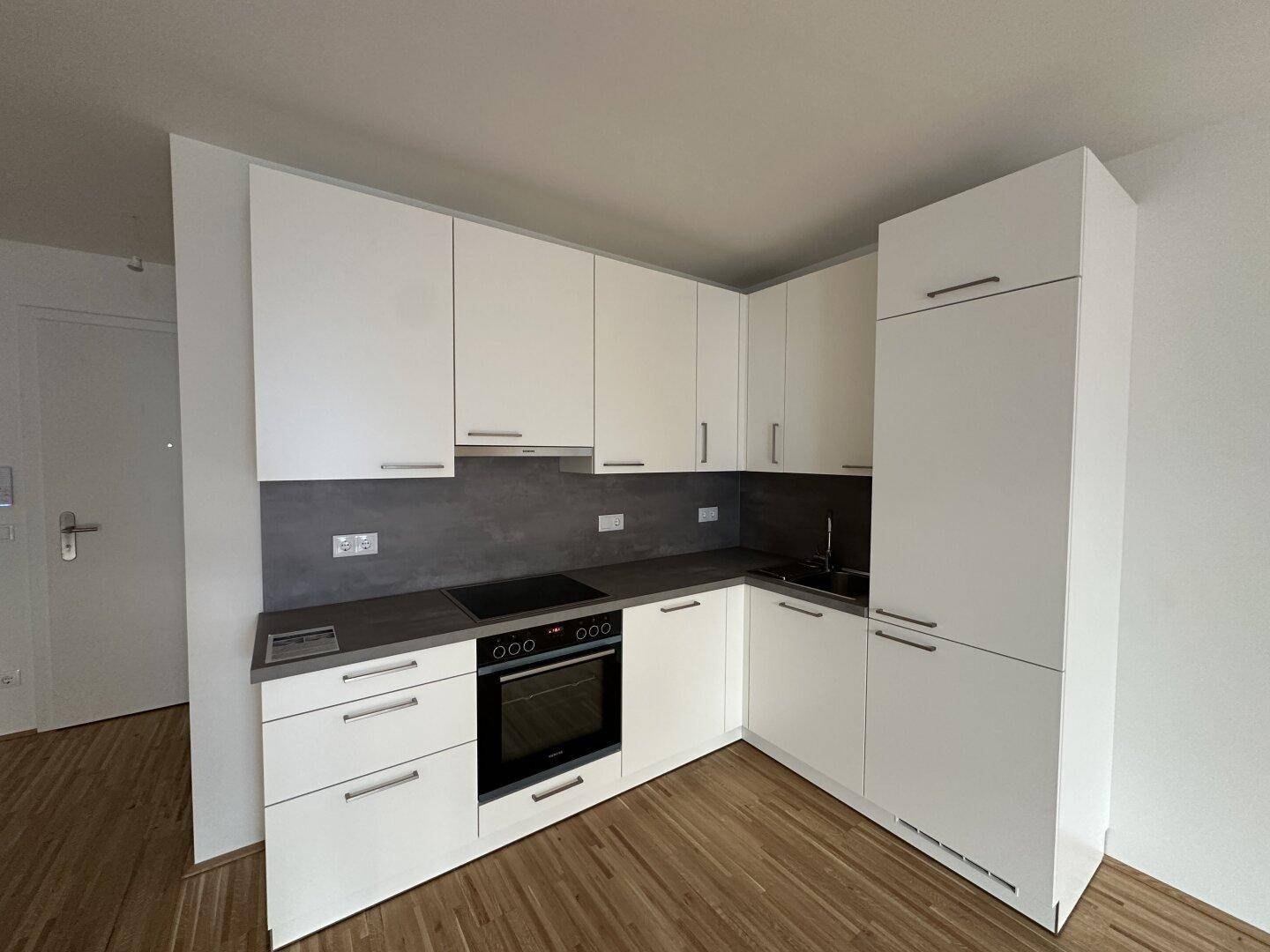 Moderne Einbauküche mit weißen Schränken, dunkler Arbeitsplatte und integrierten Geräten.