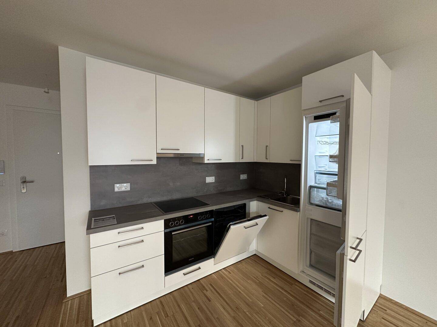 Voll ausgestattete moderne Küche mit weißen Fronten, Backofen und integriertem Kühlschrank.