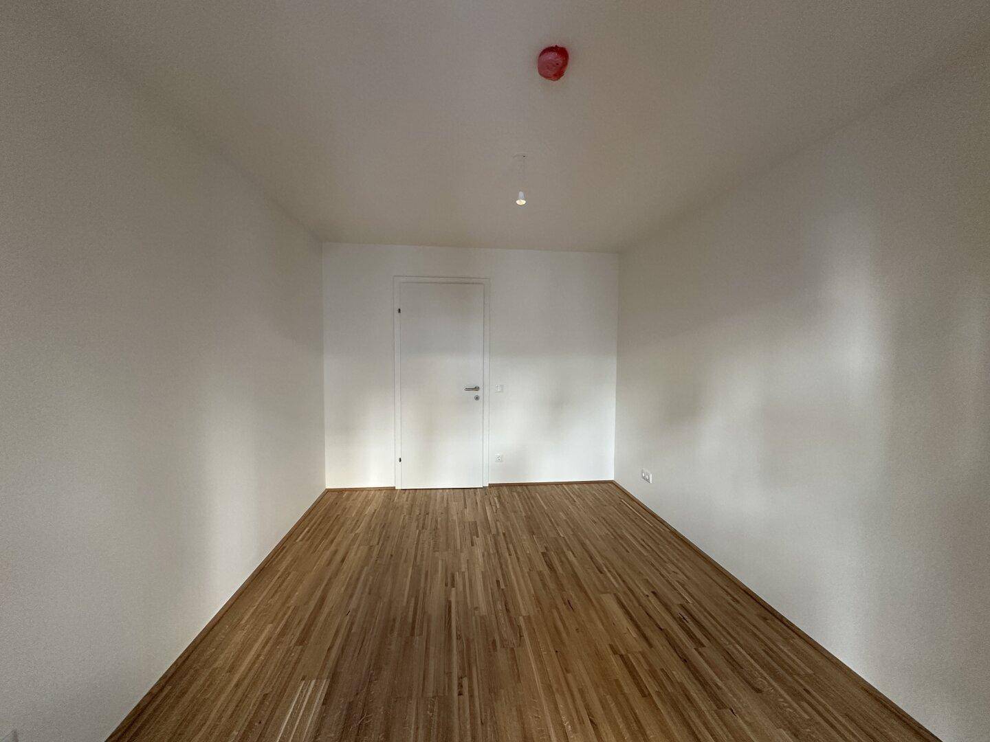 Leeres Zimmer mit Parkettboden und einer weißen Tür, bereit zur individuellen Gestaltung.