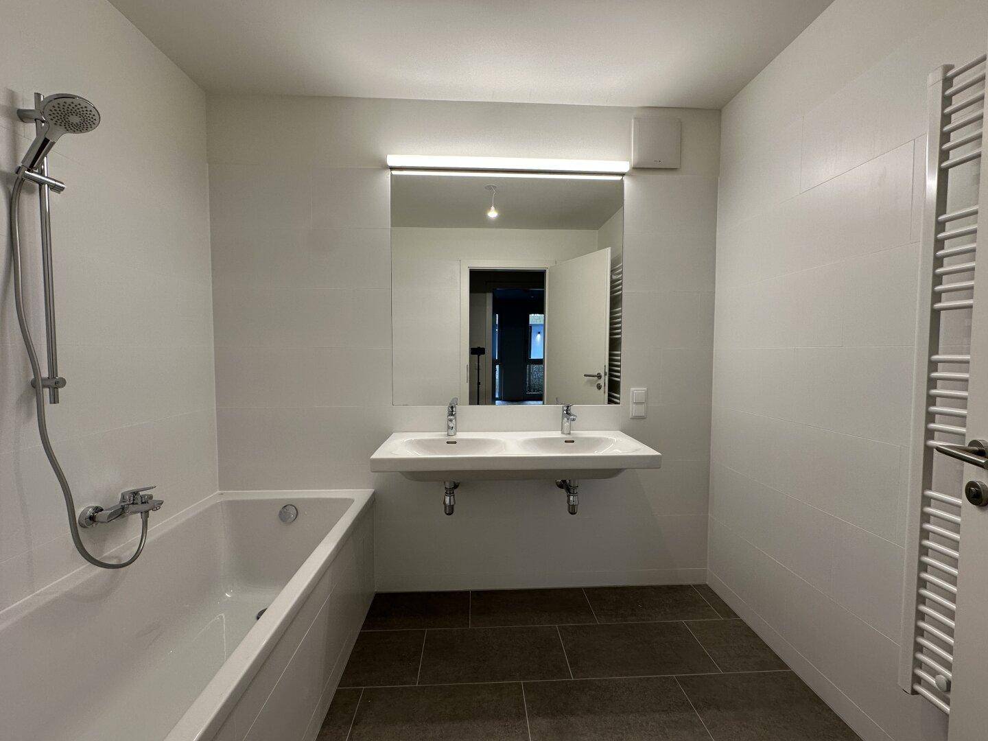 Modernes Badezimmer mit Badewanne, Doppelwaschbecken und beheiztem Handtuchhalter.