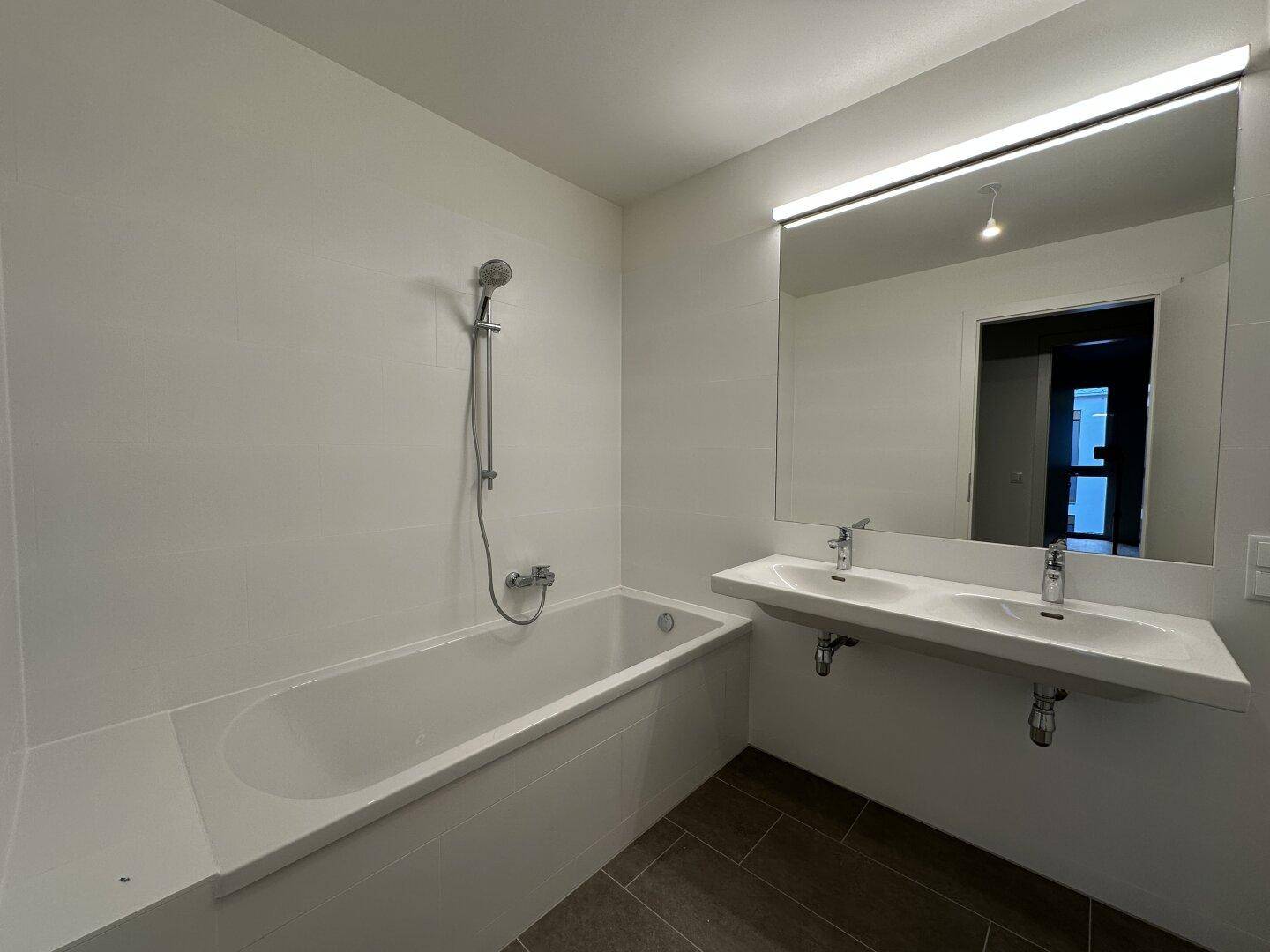 Helles Badezimmer mit Badewanne, Doppelwaschbecken und großem Spiegel mit Beleuchtung.