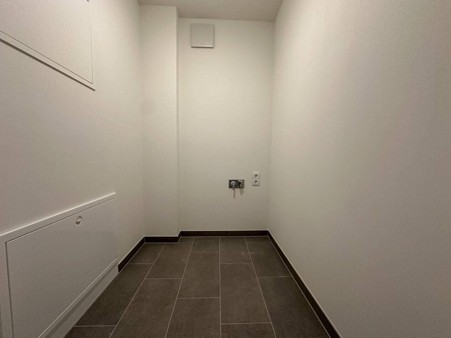 Praktischer Abstellraum mit Fliesenboden und Anschlüssen für Waschmaschine oder Trockner.