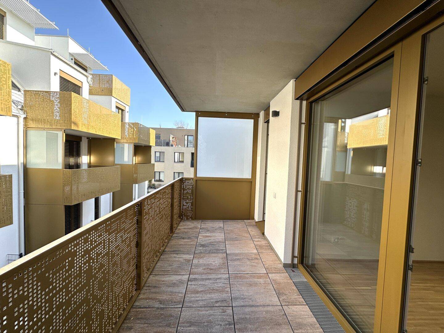 Langer Balkon mit Fliesenboden und moderner Metallbrüstung, sonnig und hell.