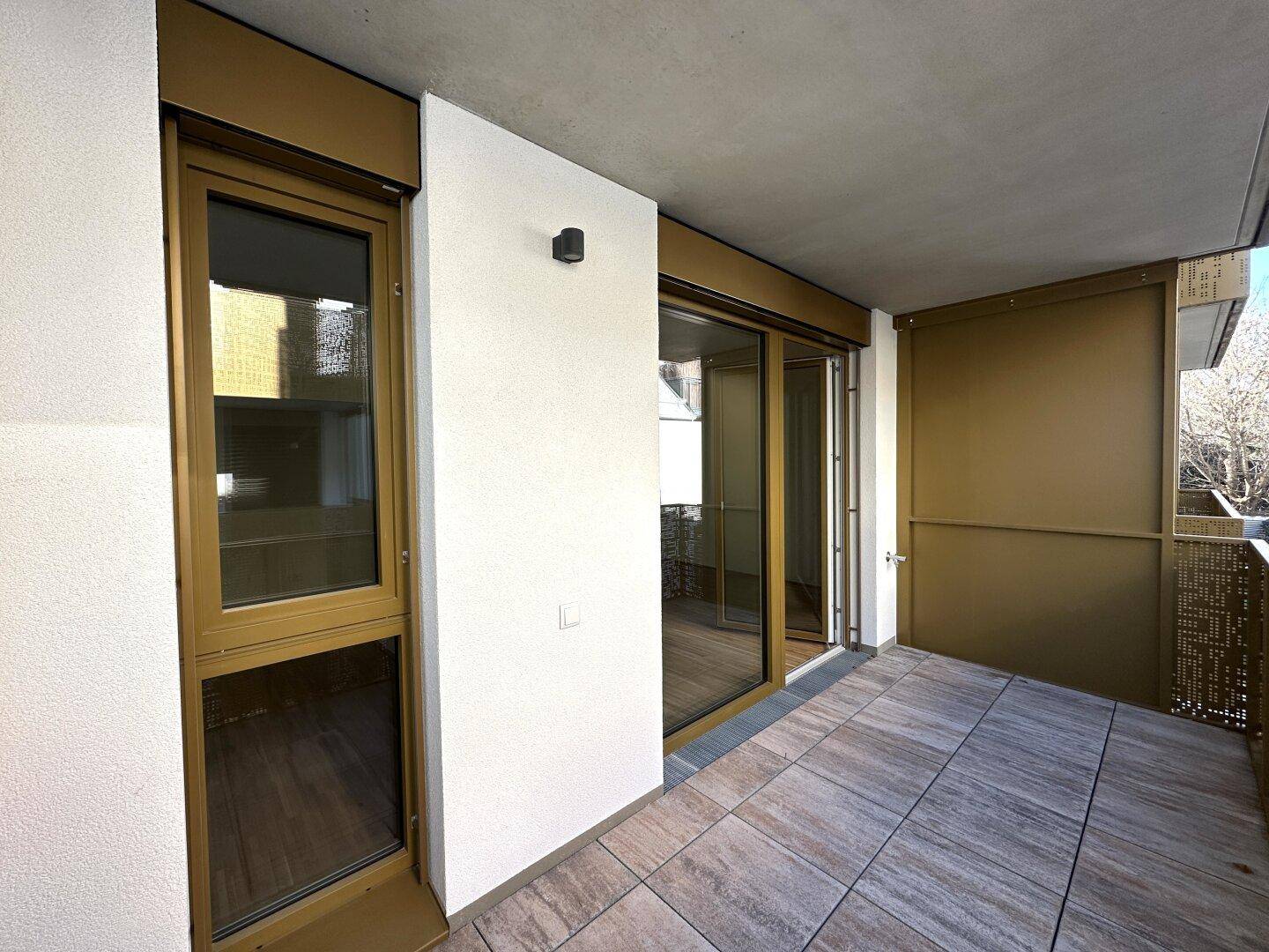 Geräumiger Balkon mit Fliesenboden und Zugang zum Innenraum durch große Glastüren.