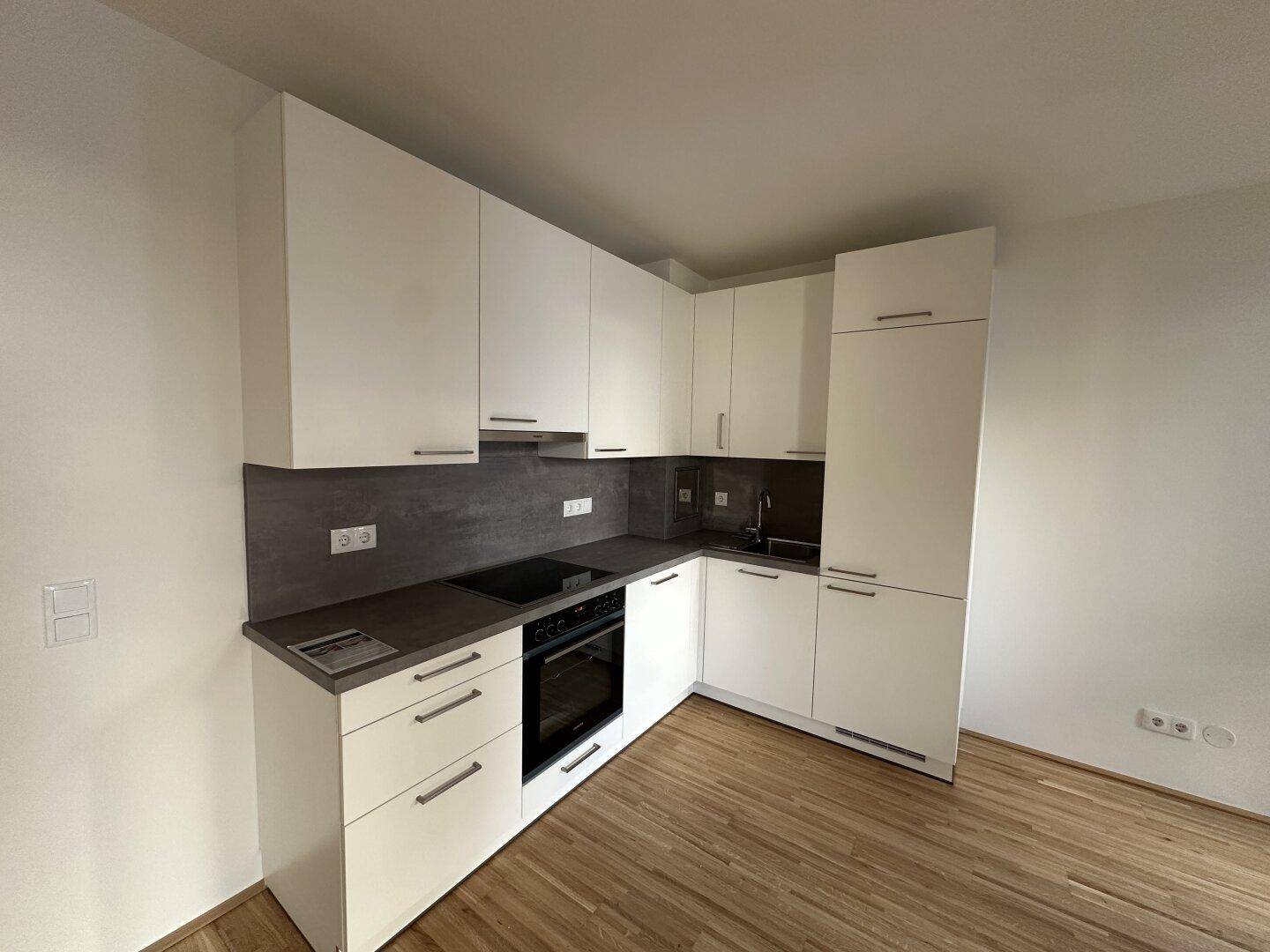 Moderne Einbauküche mit weißen Schränken, dunkler Arbeitsplatte und integrierten Geräten.