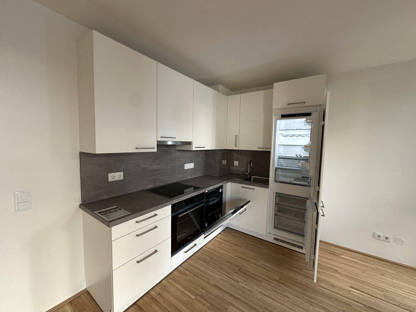 Neue Einbauküche mit Kühlschrank, Kochfeld und ausreichend Stauraum in minimalistischem Design.