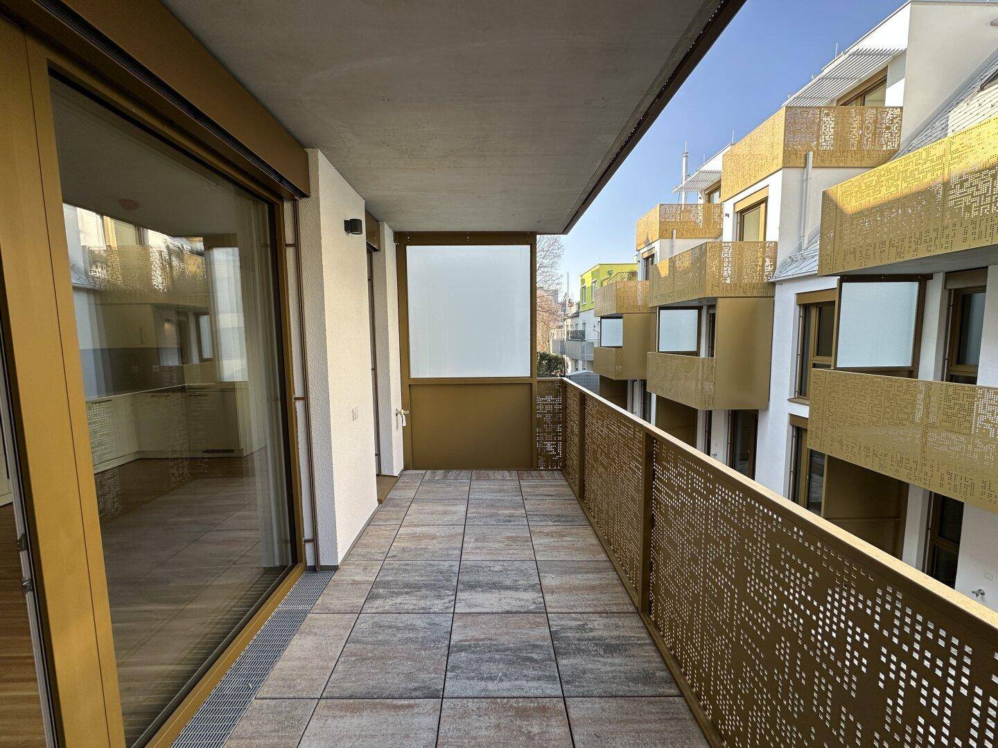 Langer Balkon mit Fliesenboden und goldfarbenem Geländer, bietet Platz für Entspannung im Freien.