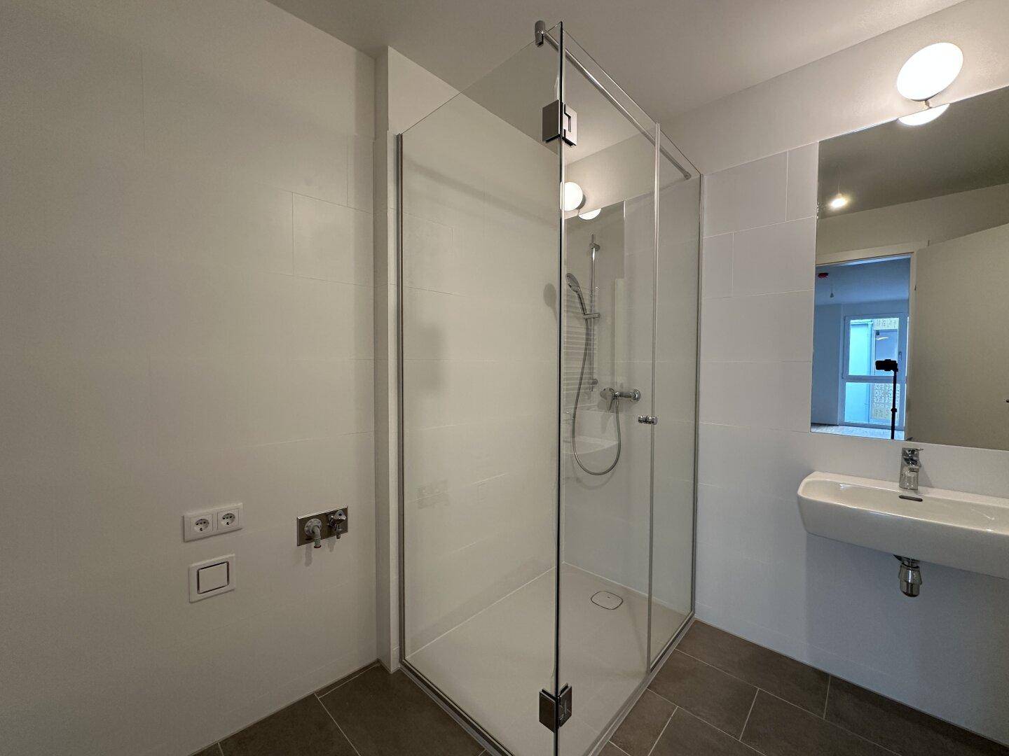 Zeitgemäßes Badezimmer mit großer Glasdusche und minimalistischem Design, hell gefliest.