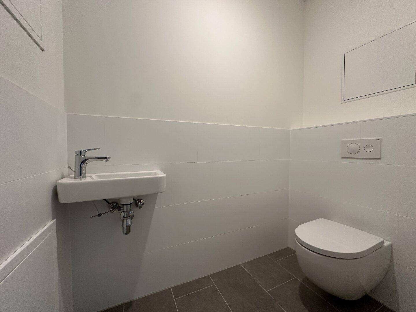 Modernes Gäste-WC mit wandhängender Toilette und kleinem Waschbecken, in neutralen Farben gehalten.