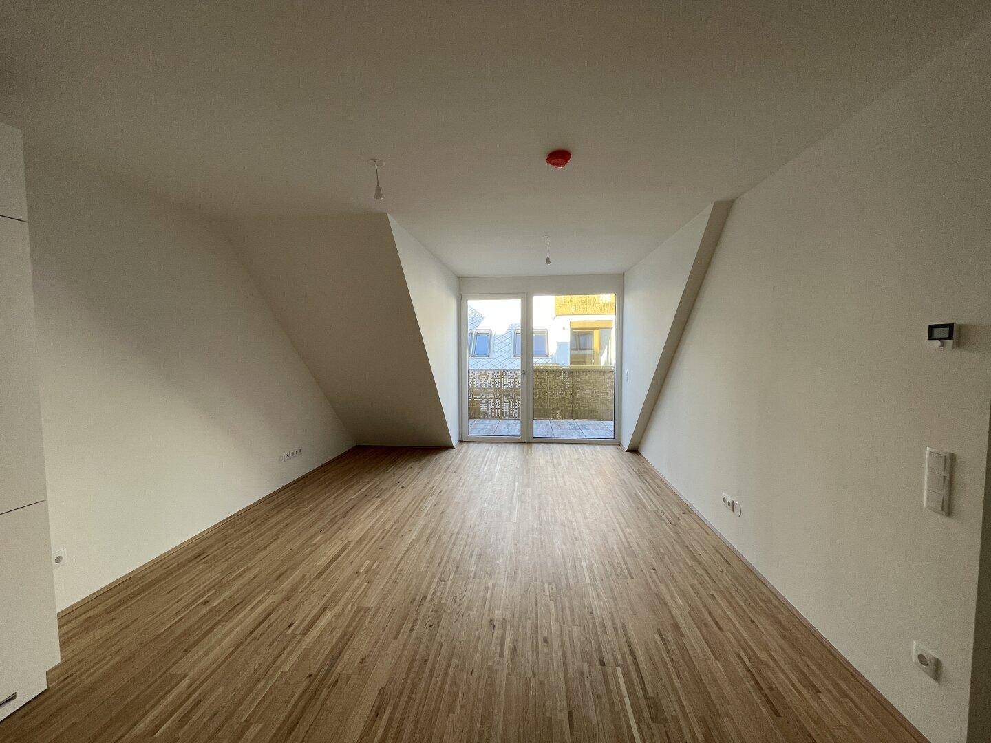 Heller Wohnbereich mit Holzboden und Zugang zu einem Balkon, ideal für entspannte Stunden.