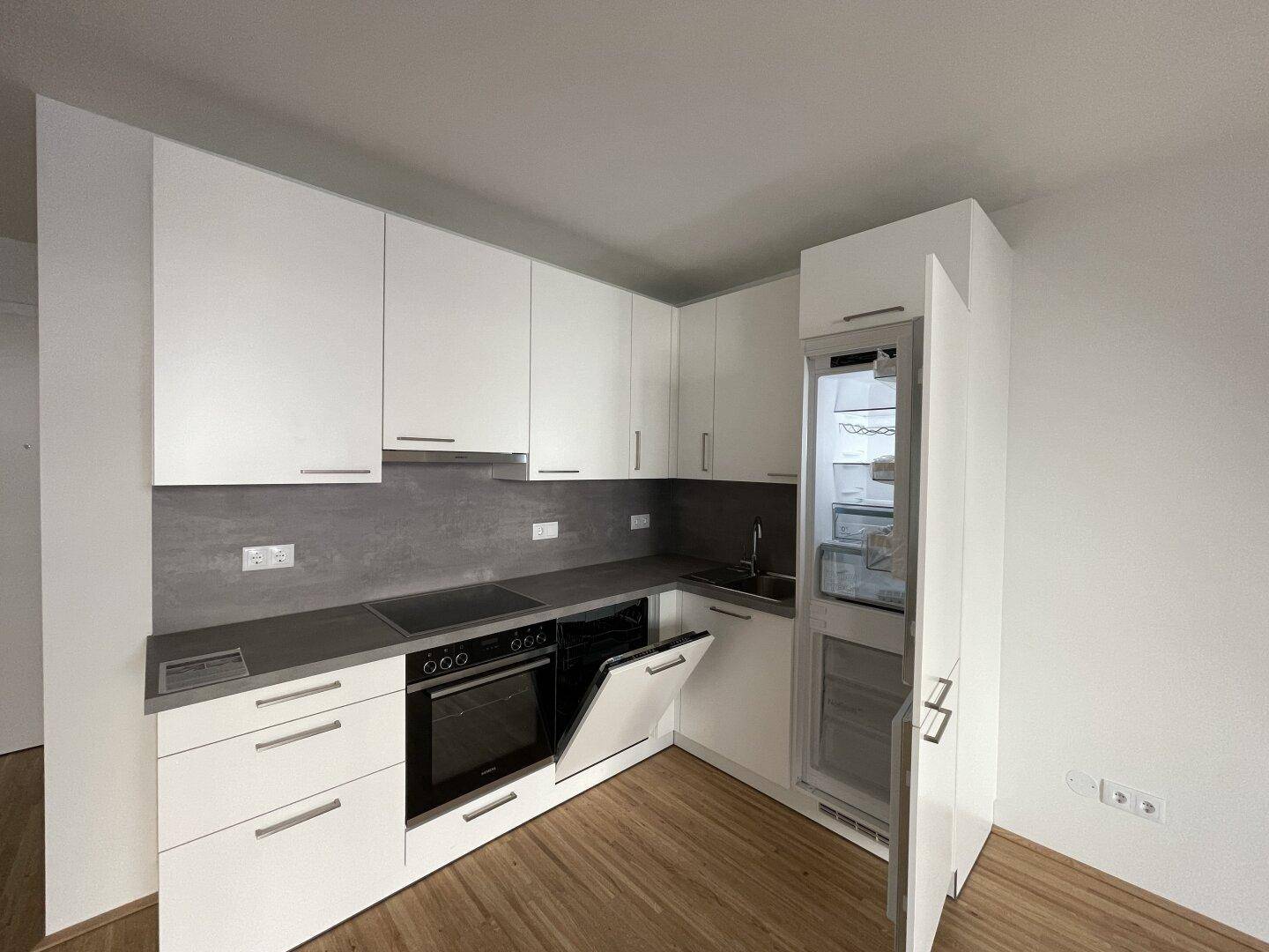 Moderne Küche mit integriertem Kühlschrank und Backofen, bereit zur ersten Nutzung.