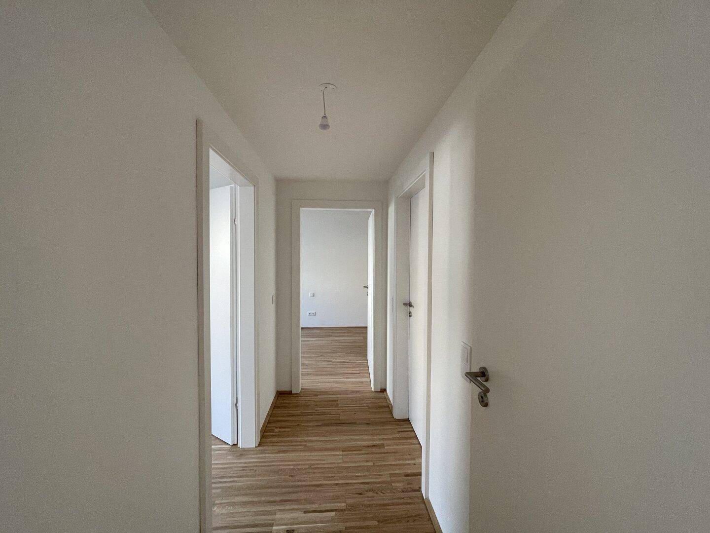 Heller Flur mit Holzboden, der zu verschiedenen Räumen der Wohnung führt.