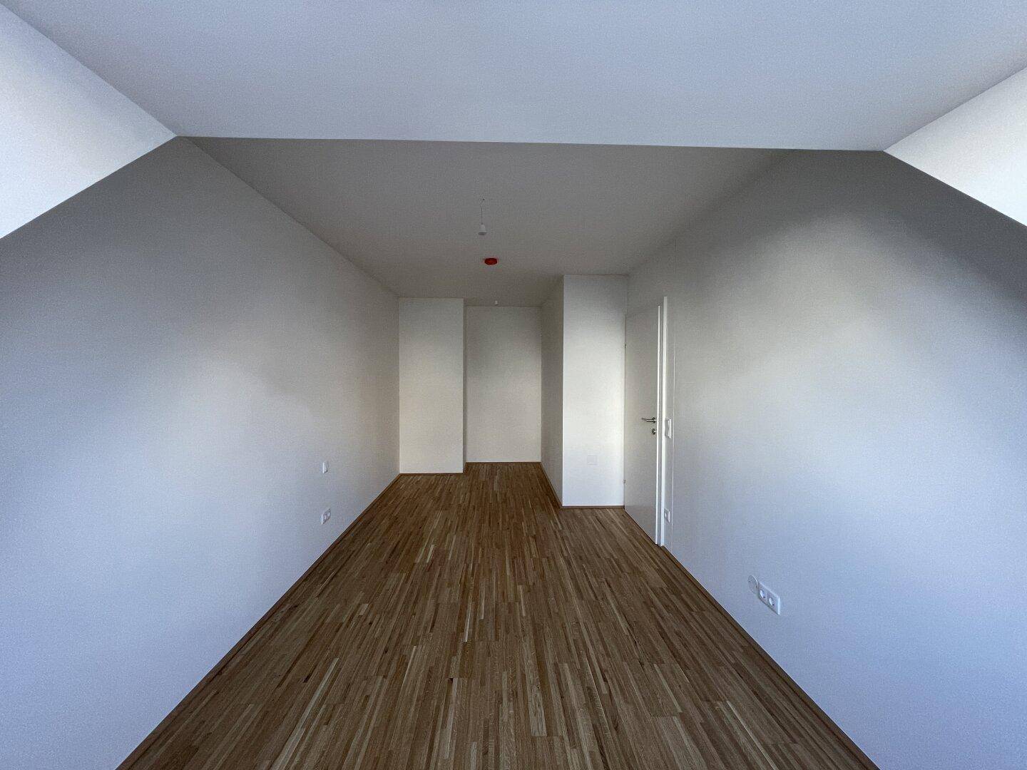Langes, helles Zimmer mit Holzboden und Dachschrägen, vielseitig nutzbar.