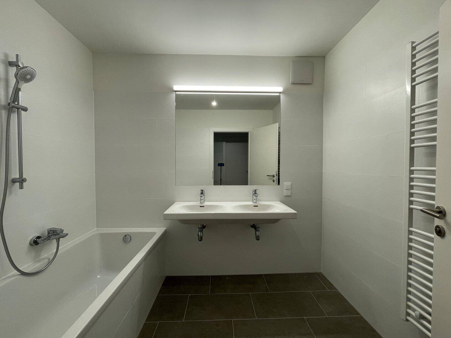 Modernes Badezimmer mit Doppelwaschbecken, Badewanne und beheiztem Handtuchhalter.