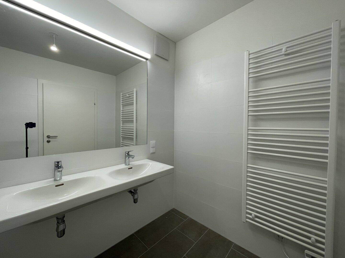 Helles Badezimmer mit Doppelwaschbecken und großem Spiegel, modern gefliest.