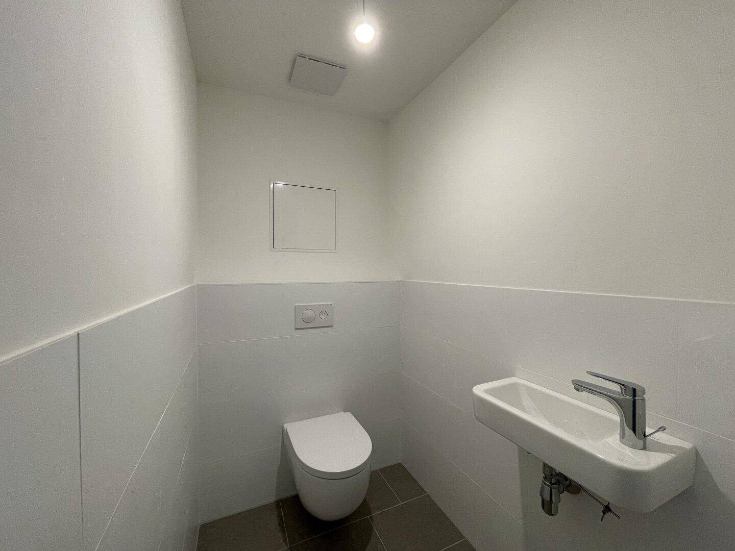 Separates Gäste-WC mit wandhängender Toilette und kleinem Waschbecken.