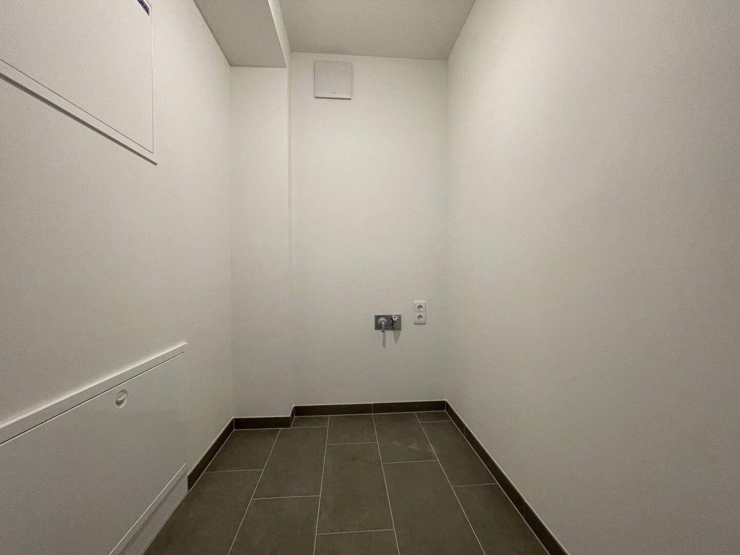 Praktischer Abstellraum mit Fliesenboden und Anschlüssen für Waschmaschine.