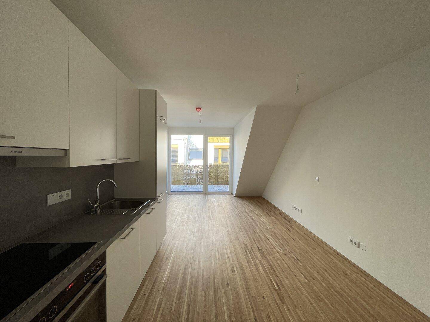 Moderne Küchenzeile in einem lichtdurchfluteten Wohnbereich mit Holzboden und Blick auf den Balkon.