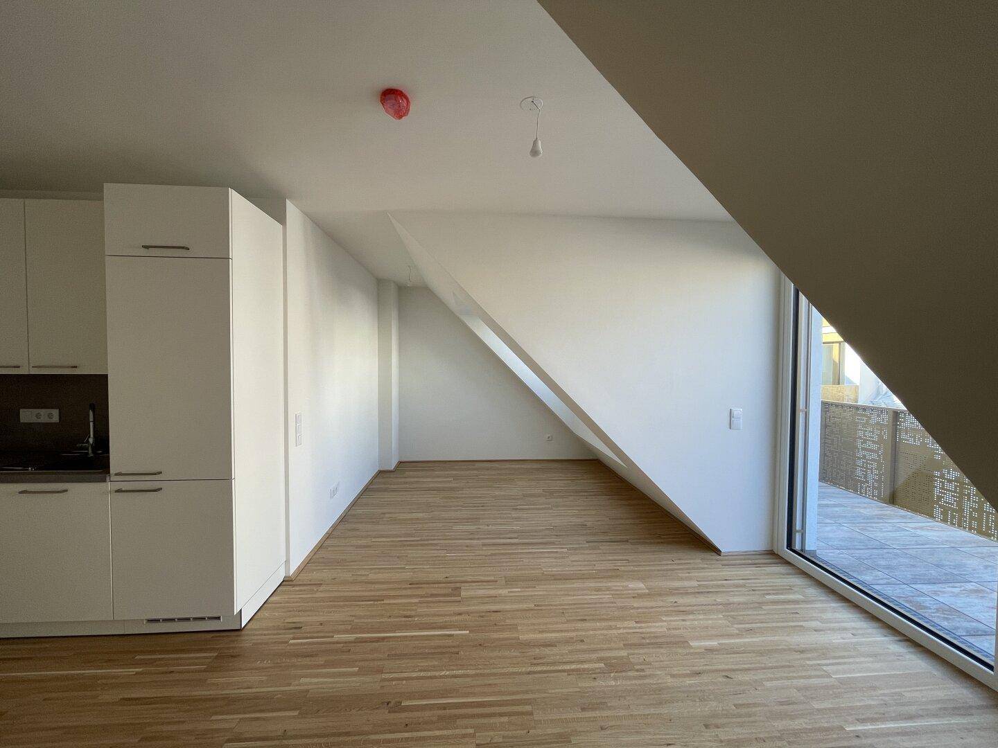 Geräumiger, heller Wohnbereich mit Holzboden und schrägen Wänden im Dachgeschoss, ideal für offenes Wohnen.