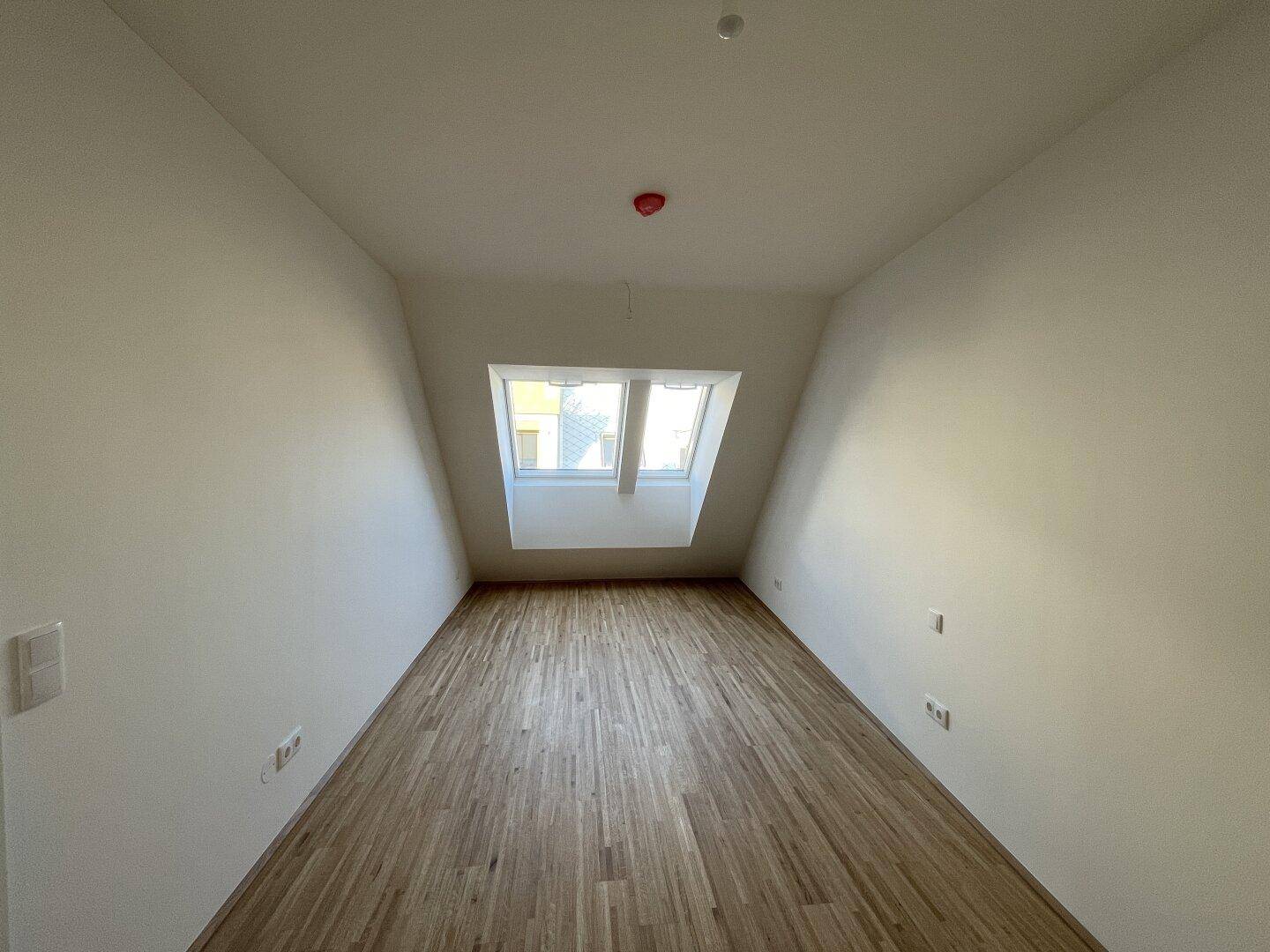 Helles Schlafzimmer im Dachgeschoss mit Holzboden und einem Fenster in der schrägen Wand, bietet viel Tageslicht.